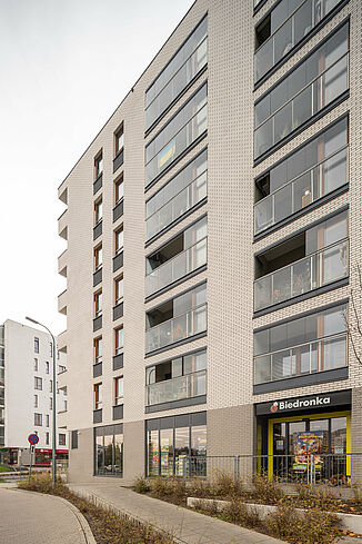 Vue latérale d'un immeuble à Varsovie avec un supermarché au rez-de-chaussée et des appartements au-dessus.