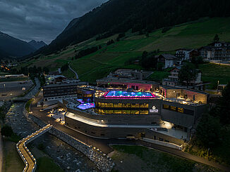 Vue frontale des thermes Silvretta illuminés à Ischgl la nuit avec les immeubles d'habitation environnants.