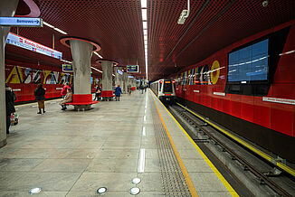 Station de métro à Varsovie avec des murs rouges à côté des voies et des bancs rouges dans la zone d'attente.