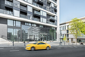 Entrée de la tour Henninger à Francfort avec une voiture jaune qui passe.