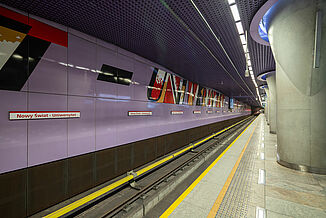 Station de métro à Varsovie avec des carreaux de céramique dans la zone d'attente et un mur de couleur violette avec des inscriptions colorées à côté des voies.