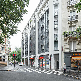 Vue extérieure d'un immeuble résidentiel et commercial à Paris, avec un supermarché Monoprix en bas et des appartements au-dessus.