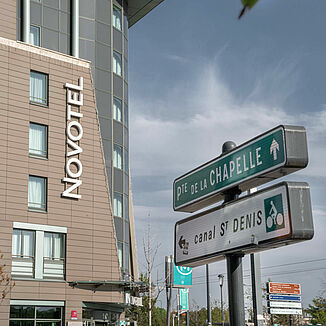 Panneaux de signalisation à Paris avec la façade de l'hôtel Novotel en arrière-plan.