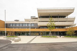 Vue de face du campus Aaron Mencer à Vienne avec une façade en bois, béton et verre et des terrasses tout autour. sur plusieurs étages.