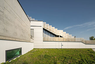 Vue extérieure avec façade en béton et escaliers menant aux terrasses du campus éducatif Seestadt Aspern à Vienne.