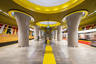 Salle d'attente avec des accents de couleur jaune sur les murs, les plafonds et les lampes dans une station de métro à Varsovie.