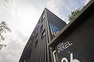 Façade noire avec publicité et fenêtres d'un bâtiment du Pôle PIXEL, immeuble de bureaux et de commerces en France.