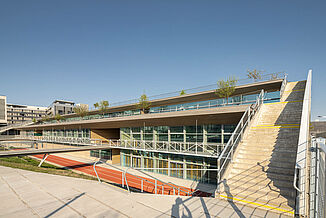 Partie de bâtiment du Seestadt Aspern Campus à Vienne avec plusieurs terrasses et une piste de course devant le bâtiment.