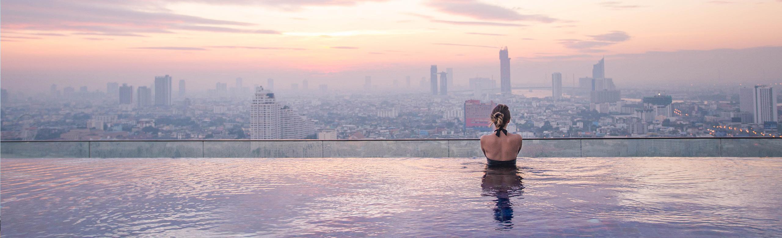 Une femme se tient dans une piscine à débordement et regarde la ligne d'horizon de la ville.